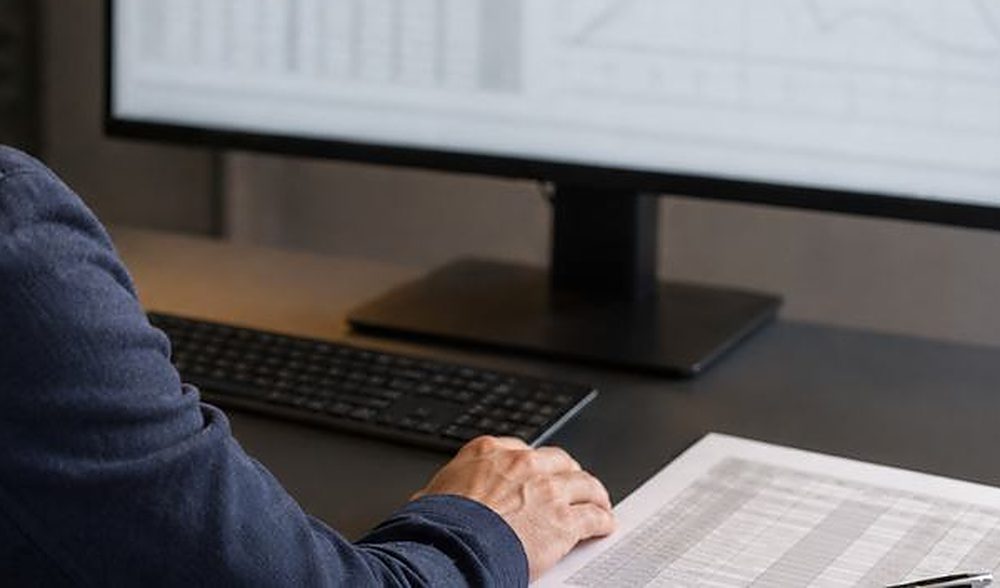 Monitor mit Tabellen und Diagramm, daneben ein ausgedruckter Bericht
